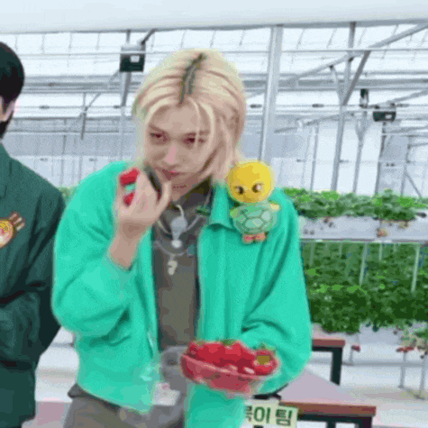 a person in a green jacket is holding a bowl of strawberries and eating one .