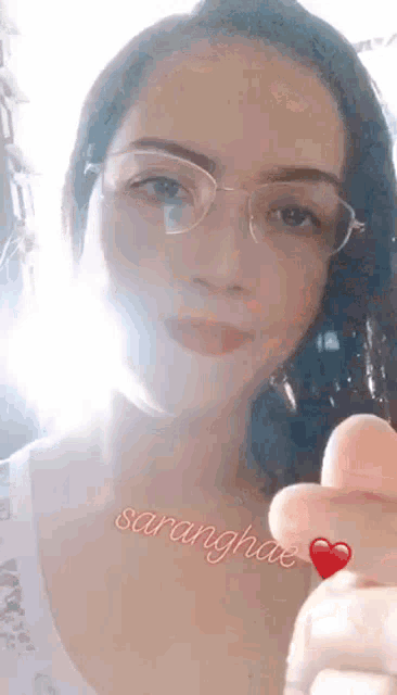 a woman wearing glasses is giving a thumbs up with a red heart on her finger .