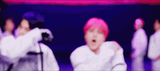 a blurry picture of a group of people with pink hair dancing in a dark room .