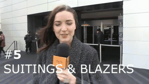a woman holding a microphone in front of a building that says suits & blazers