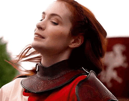 a woman with red hair is wearing a knight 's armor and smiling .