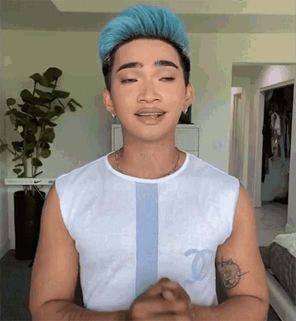 a man with blue hair is wearing a white tank top with a chanel logo on the sleeve
