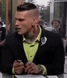 a man wearing a black jacket and a neon green shirt is sitting at a table looking at his phone