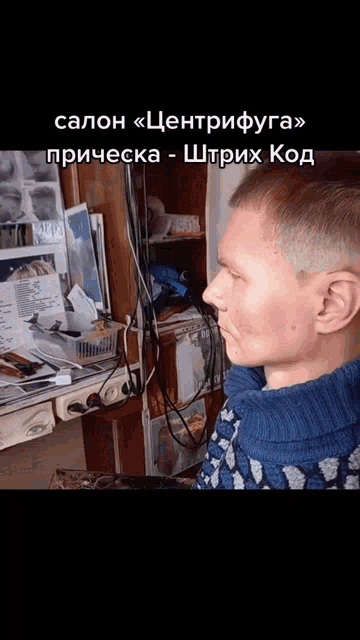 a man in a blue sweater is sitting in front of a desk with foreign writing on it