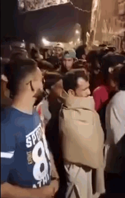 a man wrapped in a blanket is standing in a crowd of people at a party .