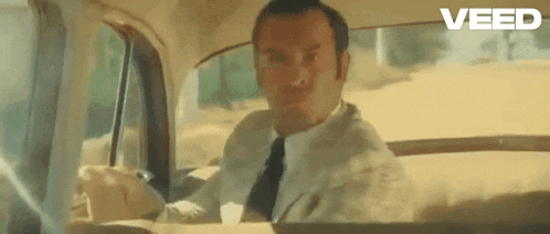 a man in a suit and tie is driving a car and making a funny face .