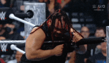 a wrestler with dreadlocks is in a wrestling ring holding a shield .