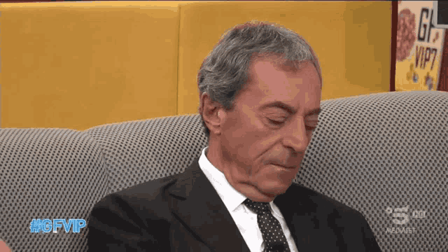 a man in a suit and tie is sitting on a couch with #gfvip written on the bottom right