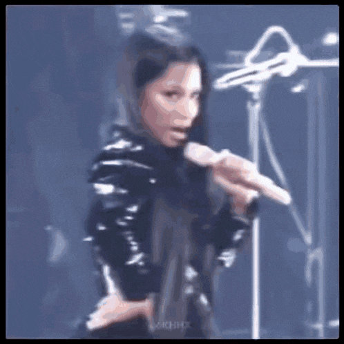 a woman in a black leather jacket is singing into a microphone on stage .