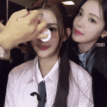 a woman is applying makeup to another woman 's face with a sticker that says ( ) on it