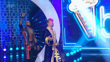 two wrestlers are standing on a stage with a trophy in the background