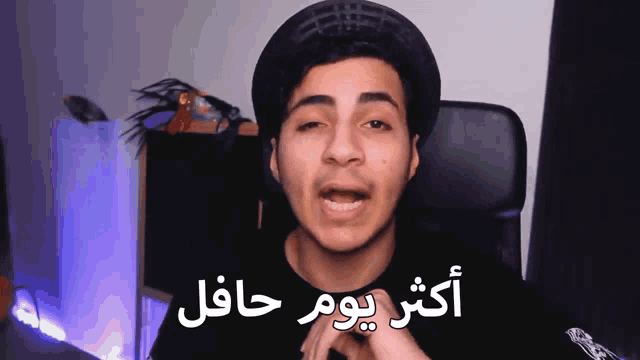 a young man wearing a hat and a black shirt is talking in arabic