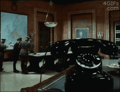 a group of men are standing around a table in a room with a telephone in the foreground