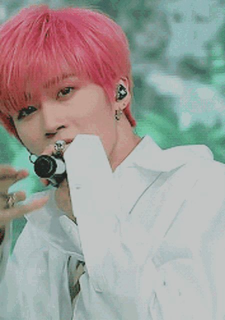 a young man with pink hair is singing into a microphone