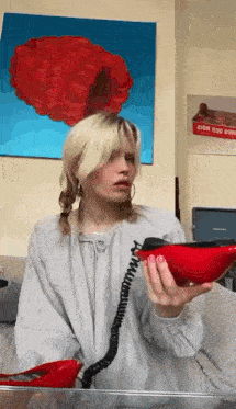 a woman is talking on a red phone in front of a painting of a raspberry on the wall .