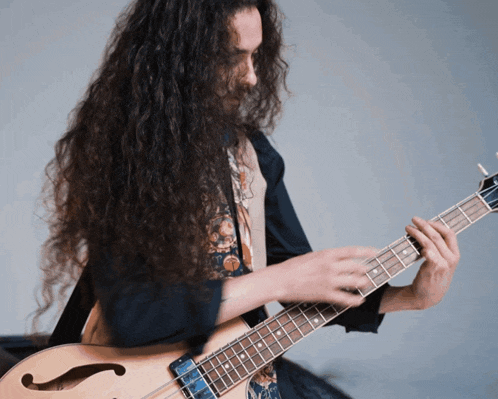 a man with long curly hair playing a bass guitar