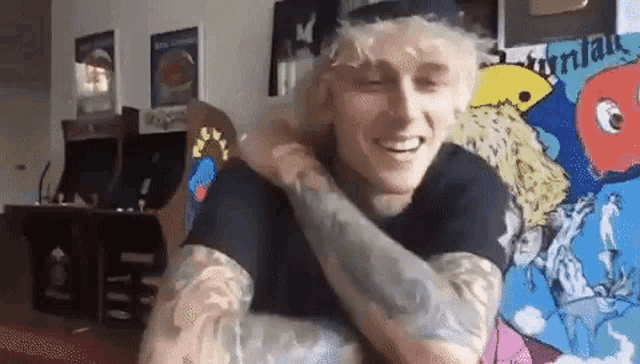 a man with a lot of tattoos on his arms is sitting in a living room with a painting on the wall .