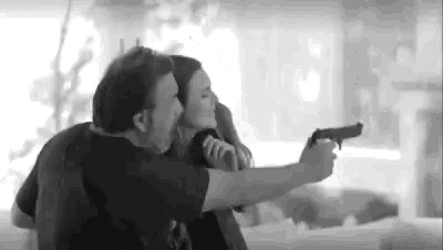 a man is pointing a gun at a woman who is holding him .
