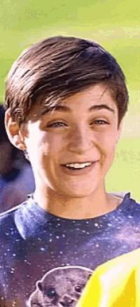 a young boy wearing a galaxy t-shirt is smiling and looking at the camera .