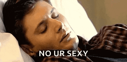 a man is sleeping in a bed with his eyes closed and the words `` no ur sexy '' written next to him .