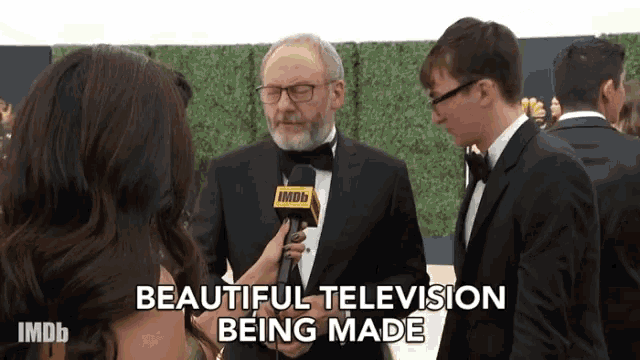 a man in a tuxedo is being interviewed by a woman with the words beautiful television being made behind him