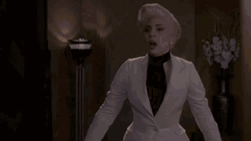 a woman in a white suit and black tie is dancing in a room .