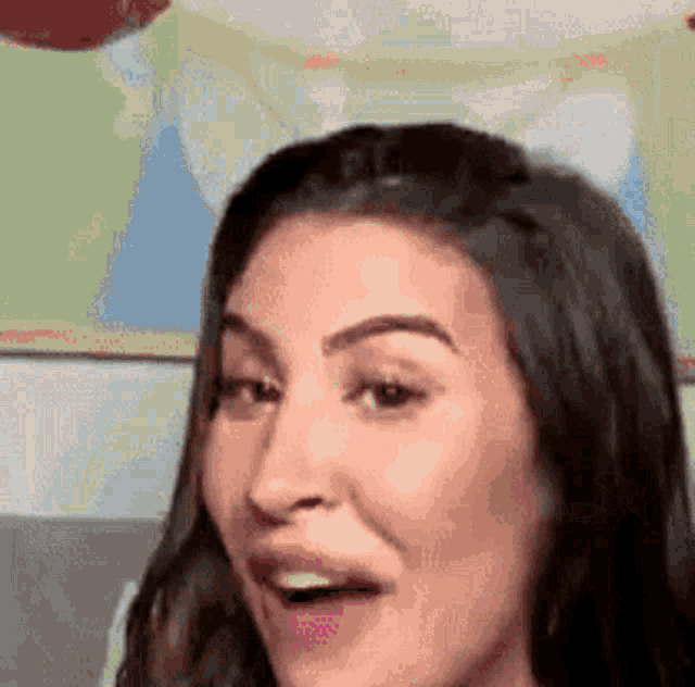 a close up of a woman 's face with her mouth open and a balloon in the background .