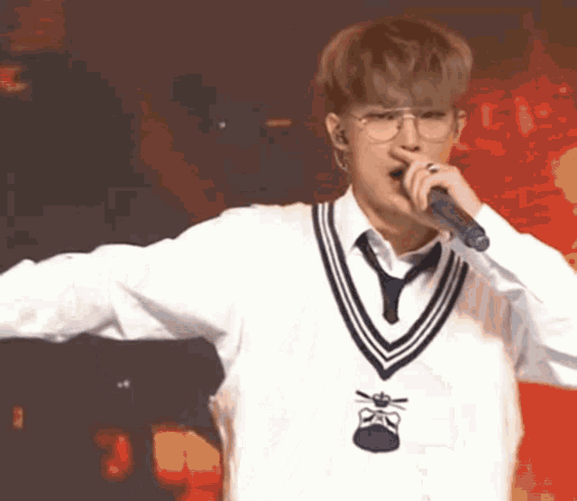 a young man is singing into a microphone while wearing glasses and a vest .