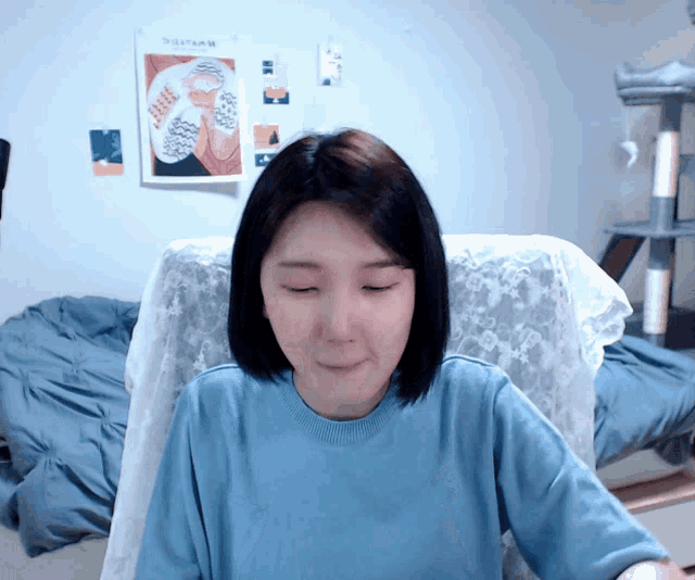 a woman wearing a blue shirt is sitting in front of a wall with a poster that says ' afternoon '