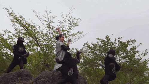 a man is holding a sword while standing on a rock with two other men
