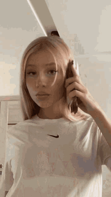 a woman wearing a white nike t-shirt is talking on her phone