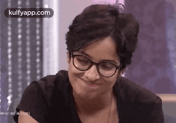 a woman wearing glasses and a black shirt is smiling and making a funny face .
