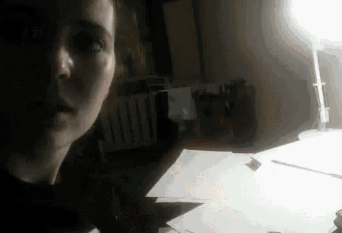 a woman is sitting at a desk in a dark room with a lamp on .