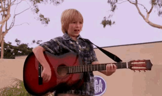 a young boy is playing an acoustic guitar outside .