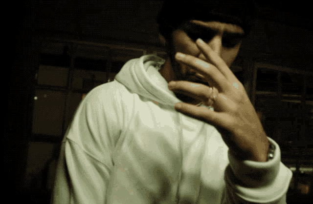 a man in a white hoodie holds his hand to his face