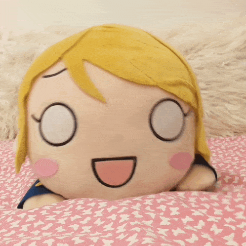 a stuffed doll with blonde hair and glasses is laying on a pink blanket