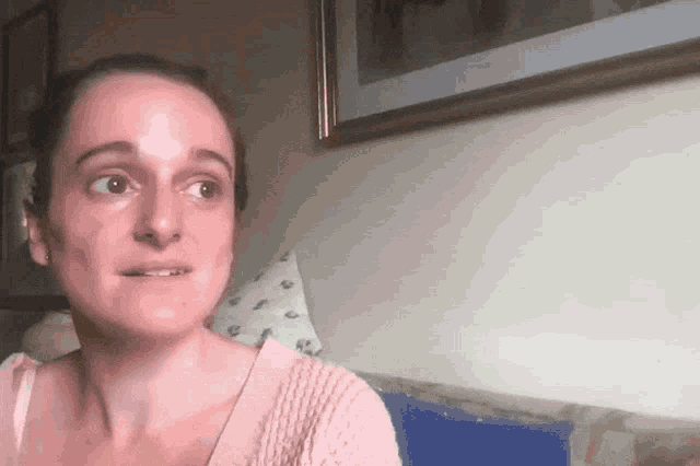a woman in a pink sweater sits on a couch in front of a picture on the wall