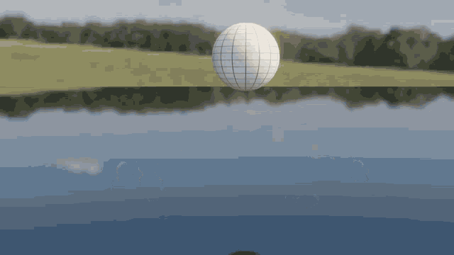a white sphere is floating in the water near a field
