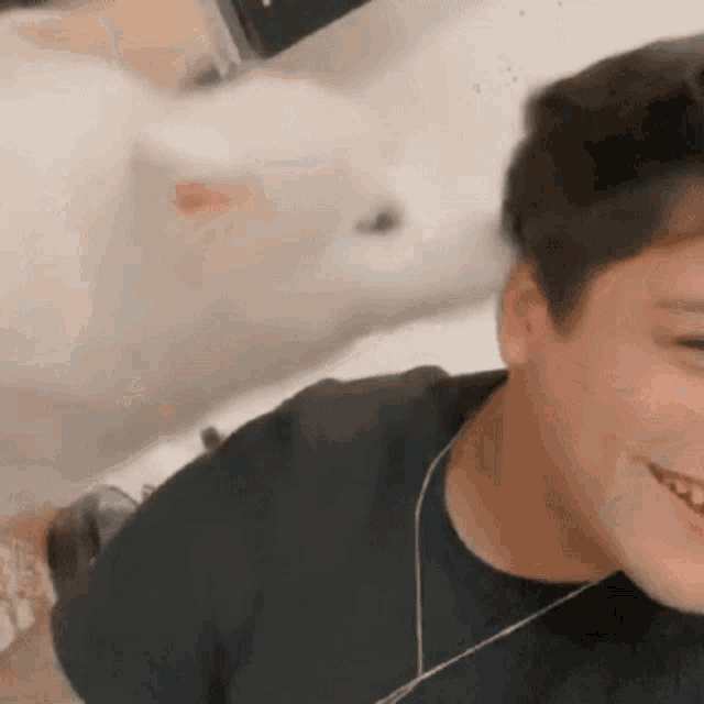 a young boy with headphones is smiling while a white cat looks on .