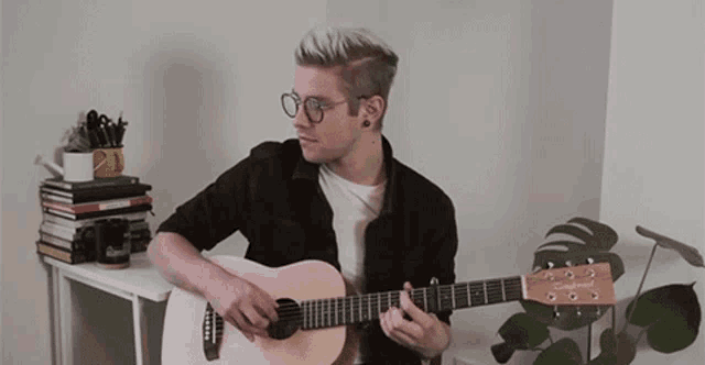 a man wearing glasses is playing an acoustic guitar in front of a plant