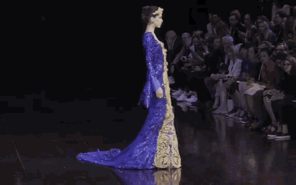 a woman in a blue and gold dress walks down the runway