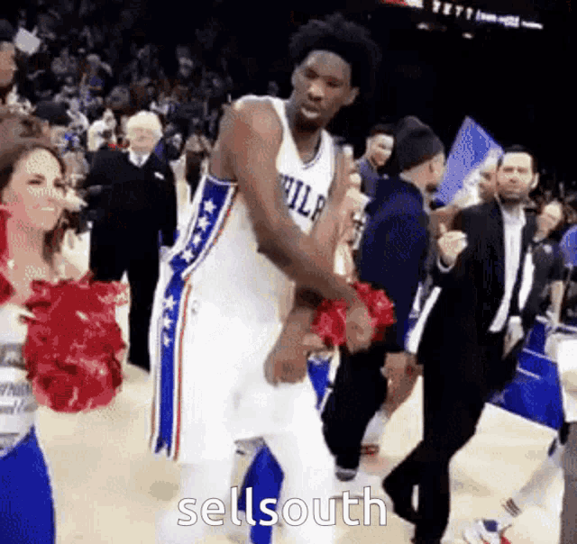 a basketball player is dancing in front of cheerleaders while wearing a jersey that says philadelphia .