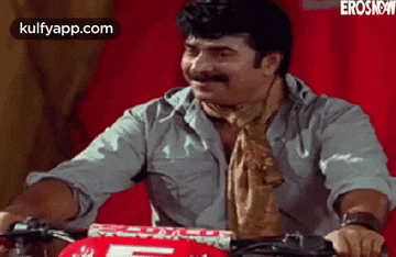a man with a mustache is sitting on a motorcycle and smiling .