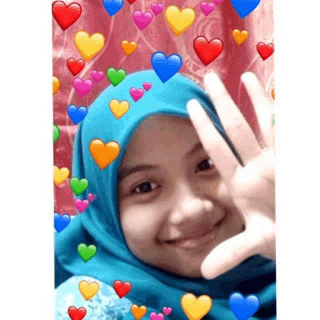 a girl wearing a blue hijab is making a heart shape with her hand