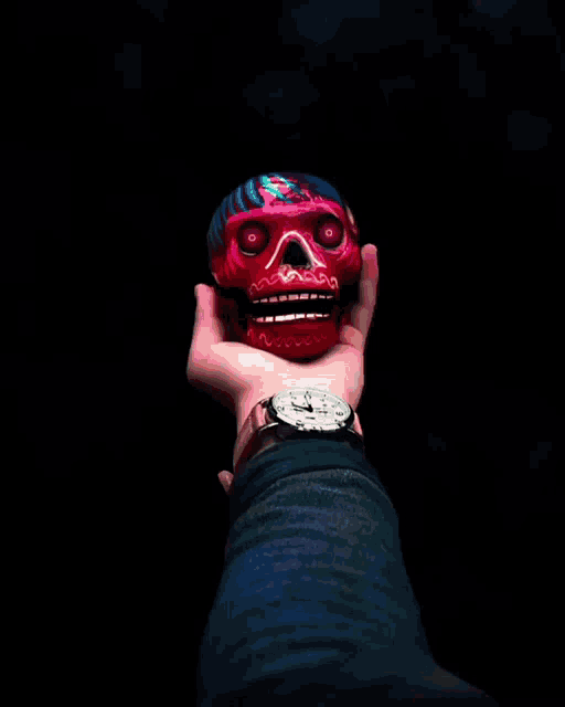 a person holding a red skull with a watch on their wrist