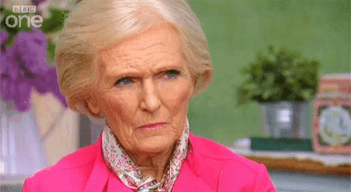 an older woman wearing a pink jacket and a scarf is making a funny face .