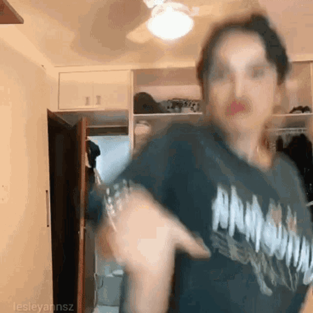 a woman in a black shirt is dancing in a room with a ceiling fan and a closet .