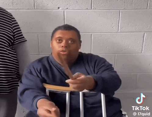 a man with down syndrome is sitting in a chair and making a funny face while holding a stick ..
