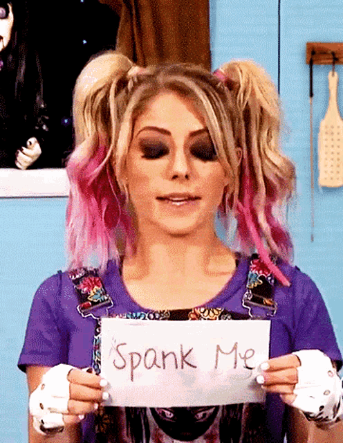 a woman with pigtails holds a sign that says spank me