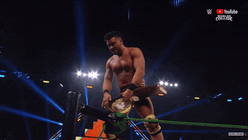 a shirtless wrestler is holding a wrestling championship belt over his head in front of a crowd sponsored by youtube